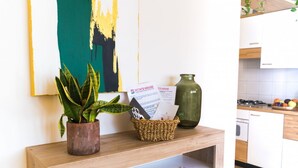 A wooden console table with a potted plant, a basket of brochures, and a vase in a modern kitchen with white cabinets and a tiled backsplash. - PELER Beth's House (Brenzone sul Garda)