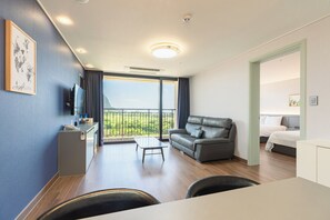 A modern hotel room with a balcony, a sofa, a desk with a telephone, and a bed. - Sanbangsan Hotel (Seogwipo)