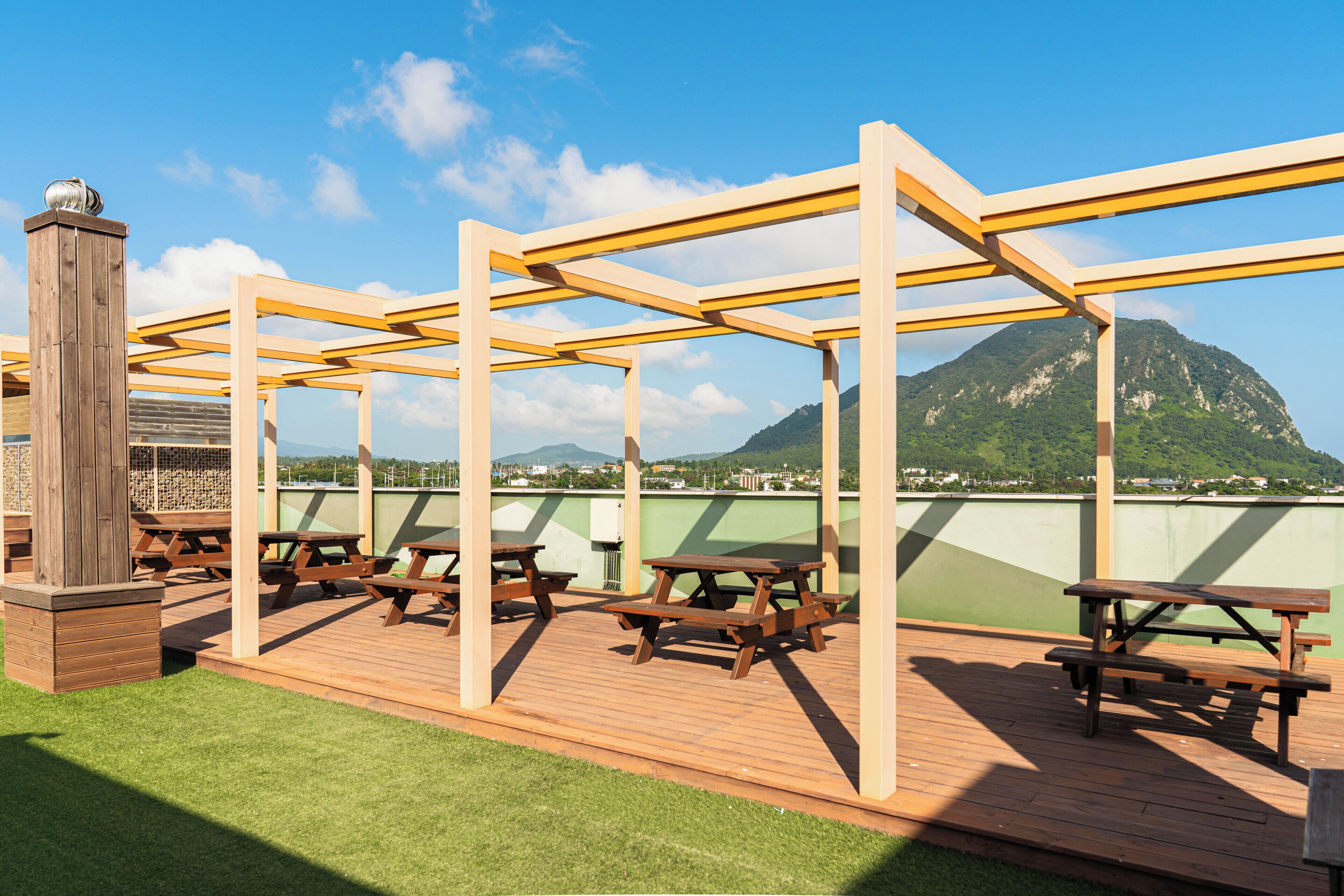 Um pátio externo com mesas de piquenique de madeira e uma estrutura de pérgola.