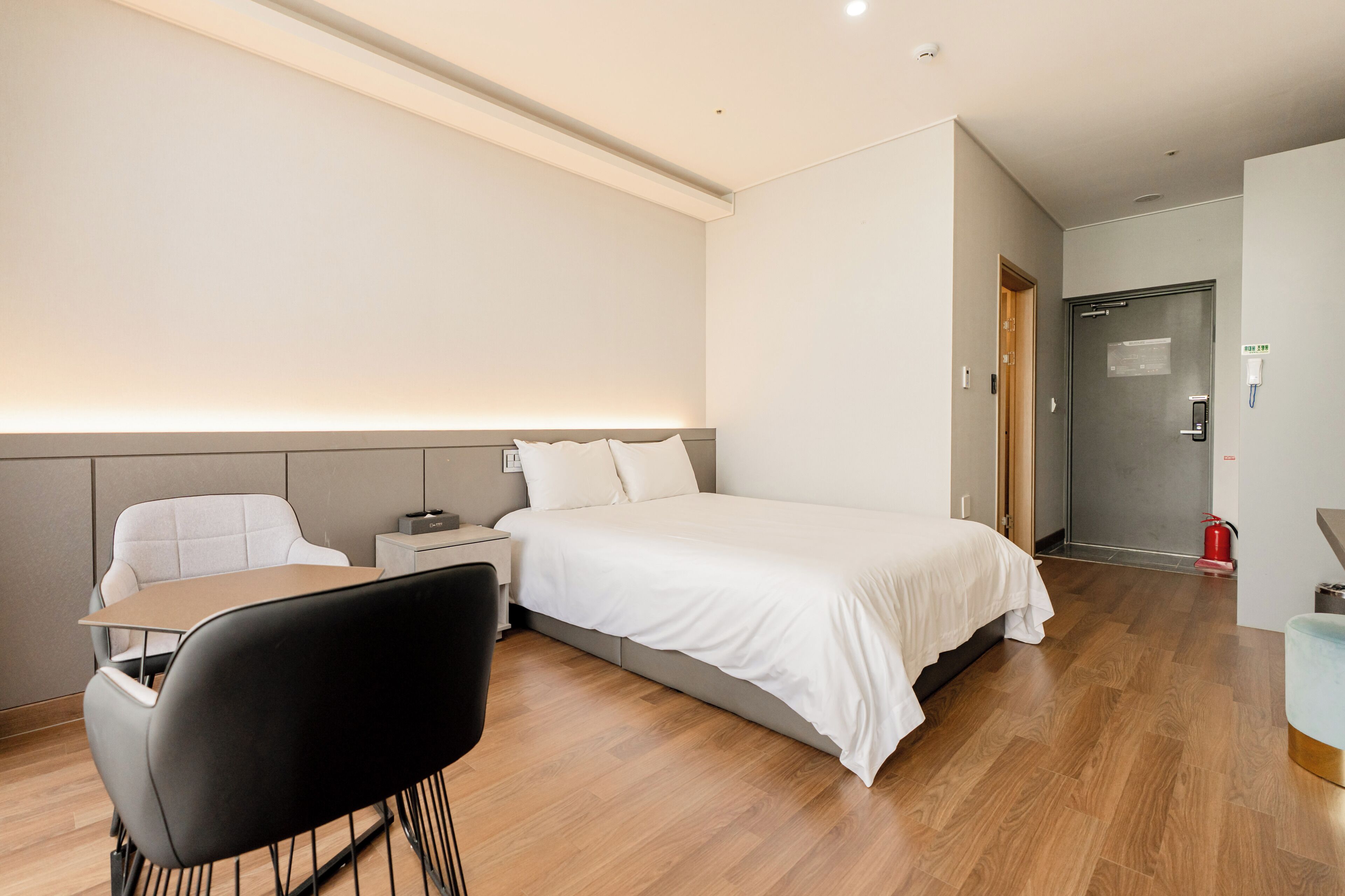 A hotel room with a bed, bedside table, chair, and a desk.
