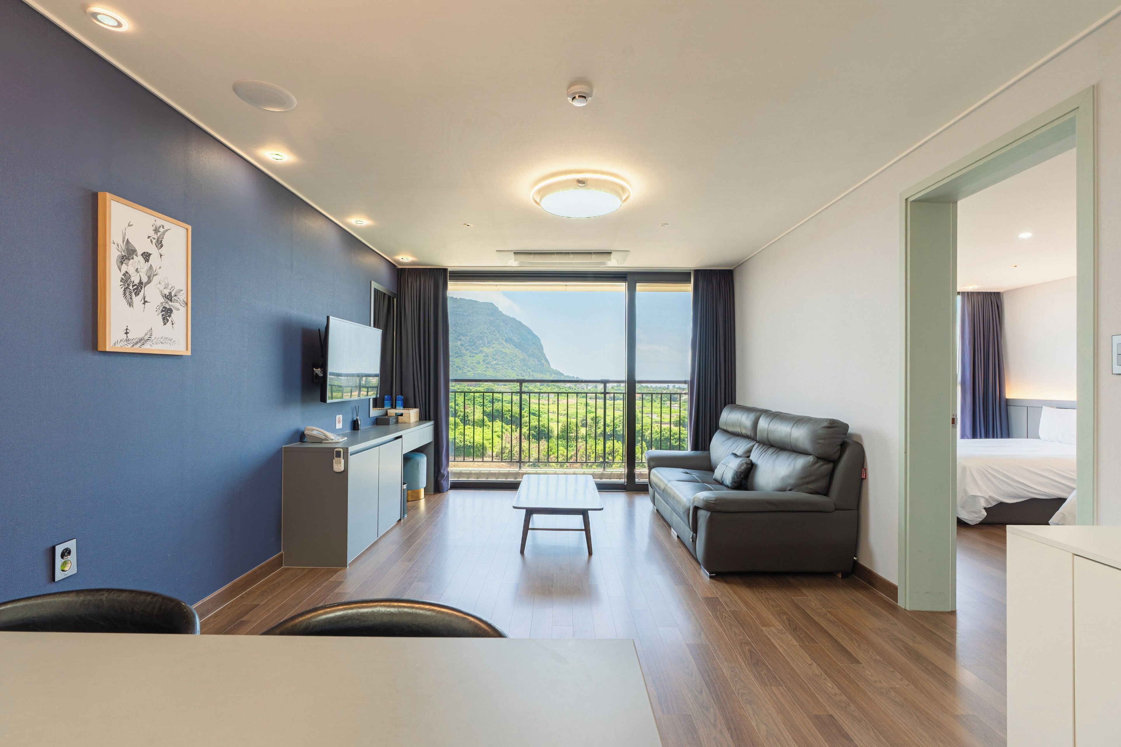Una habitación de hotel moderna con balcón, sofá, mesa de comedor y televisor.