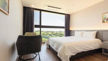 A modern hotel room with a large bed, a chair, a bedside table, and a view of the outdoors.