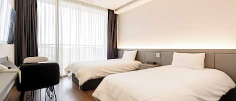 A hotel room with two beds, a desk, a chair, and a large window with curtains.