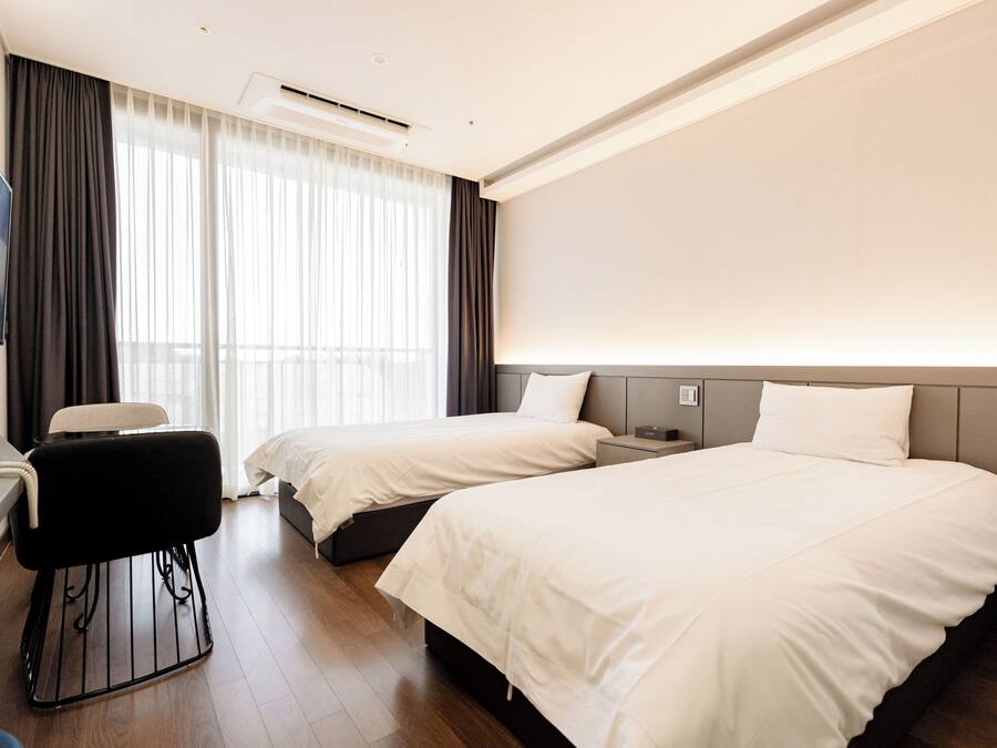 A hotel room with two beds, a desk, a chair, and a large window with curtains.