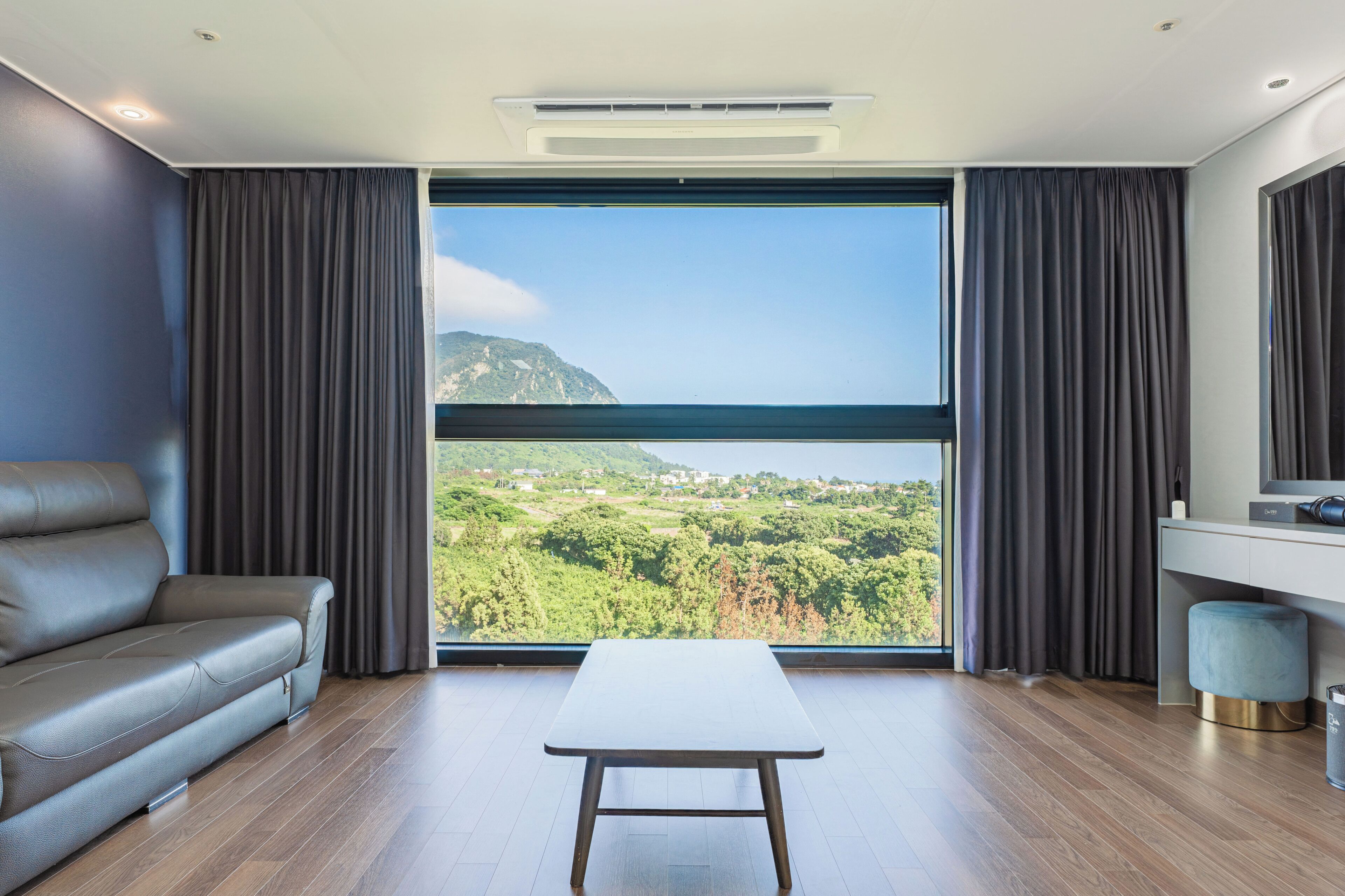 A modern room with a large window, a sofa, a table, and a small stool.