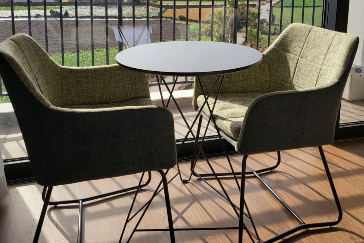 Un balcon avec deux fauteuils à revêtement vert et une petite table ronde. Le balcon offre une vue sur un paysage montagneux, avec des champs et une rivière.