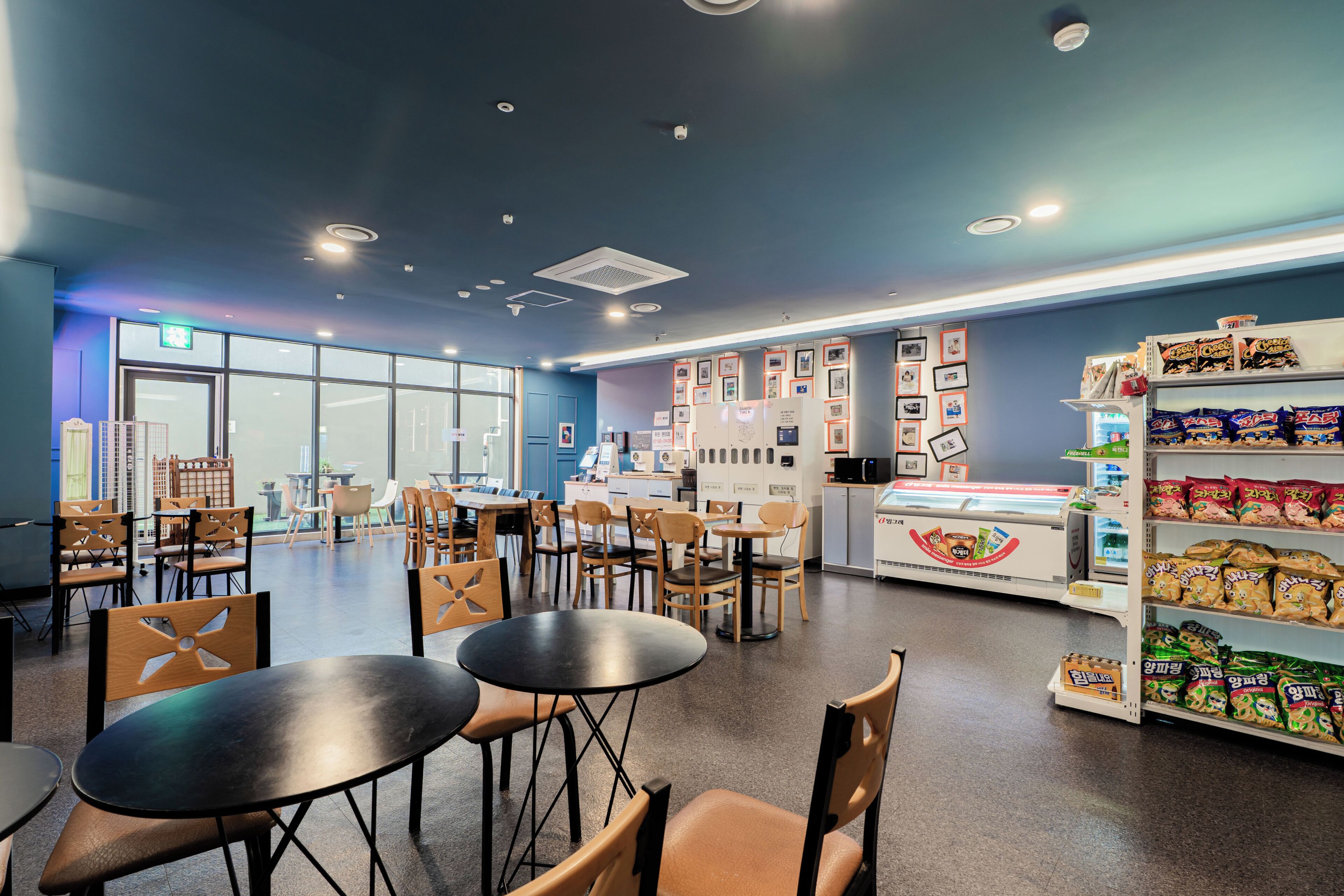 A modern cafe with tables and chairs, a display case with snacks, and a wall with framed pictures.