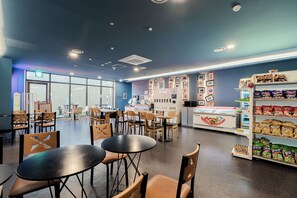 Een modern café met tafels en stoelen, een vitrine met lekkernijen en een muur met ingelijste foto's.
