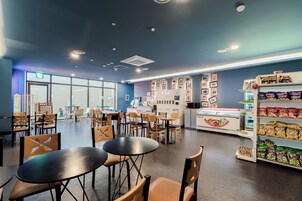 A modern cafe with tables and chairs, a display case with snacks, and a wall with framed pictures.
