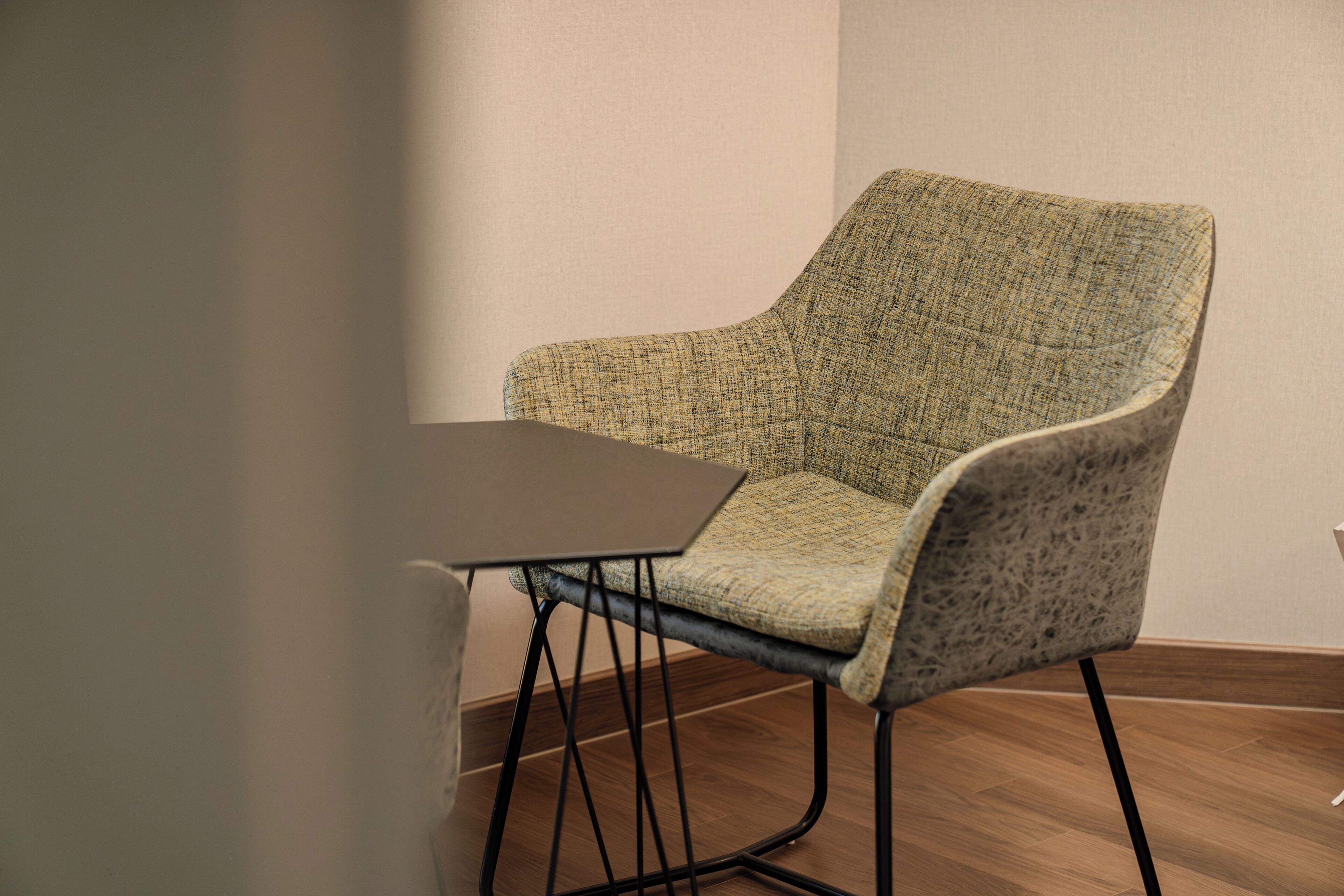 A single chair with a woven fabric seat and backrest, paired with a dark wooden table. The chair has a curved backrest and is positioned against a plain wall.