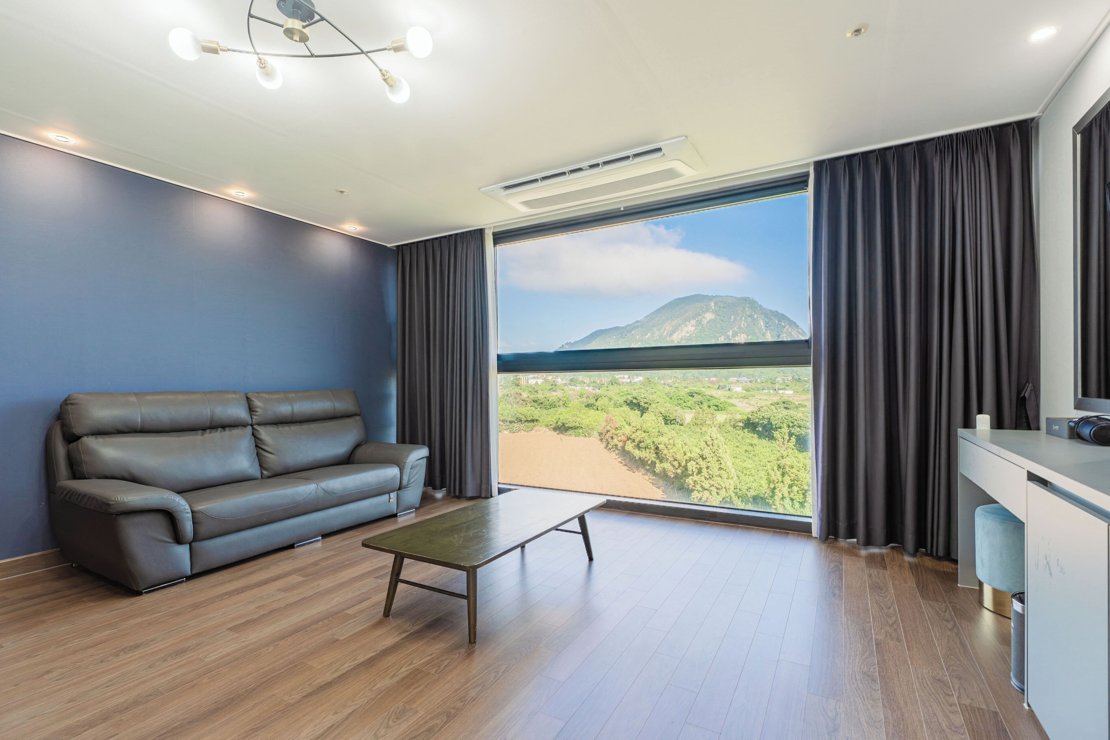 A modern living room with a leather sofa, a small table, and a large window offering a view of a mountainous landscape.