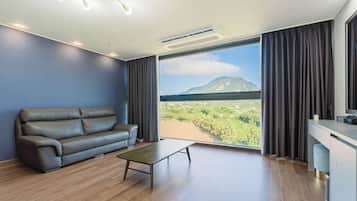A modern living room with a leather sofa, a small table, and a large window offering a view of a mountainous landscape.