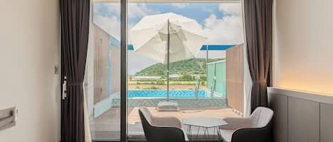 A hotel room with a sliding glass door leading to an outdoor area with a pool and umbrellas.