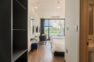 Habitación de hotel moderna con una cama grande, un escritorio con una silla, un televisor y vistas a una piscina y montañas a través de la ventana.