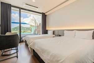A hotel room with two beds, a chair, a desk, and a view of the outdoors.