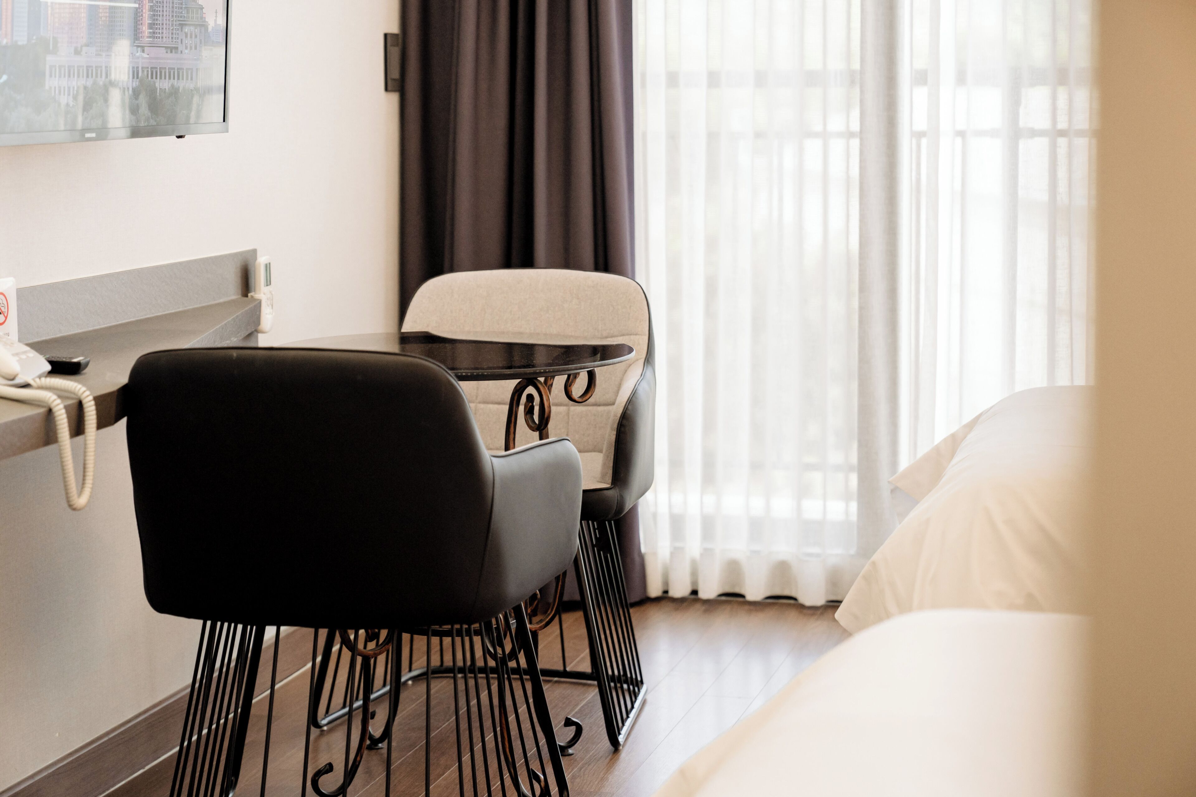 Quarto de hotel com uma cama, uma escrivaninha, uma cadeira e uma janela com cortinas.