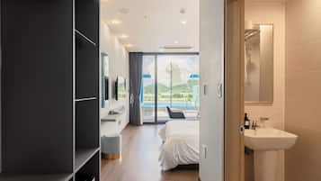 A modern hotel room with a bed, a bathroom with a sink, and a view of a pool and mountains.