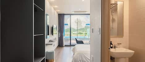 Habitación de hotel moderna con cama, baño con lavamanos y vistas a una piscina y montañas.
