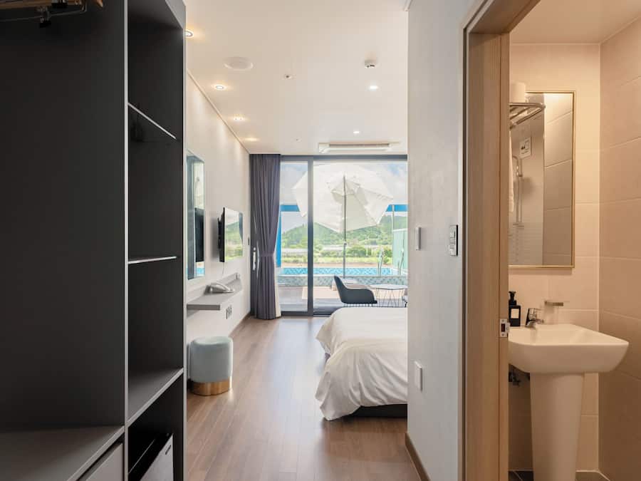 Quarto de hotel moderno com cama, banheiro com pia e vista para uma piscina e montanhas.