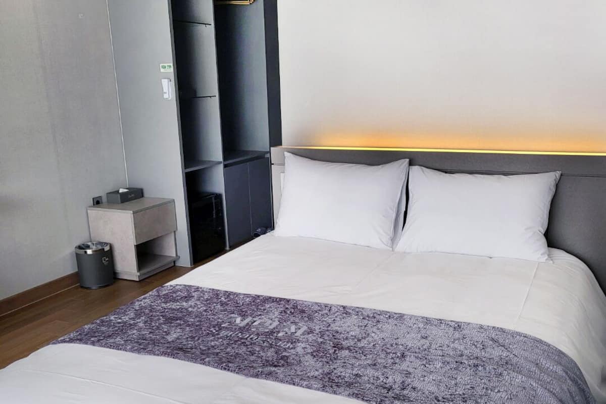 Une chambre d’hôtel moderne avec un grand lit, une table de chevet, une armoire et une lampe fixée au mur.