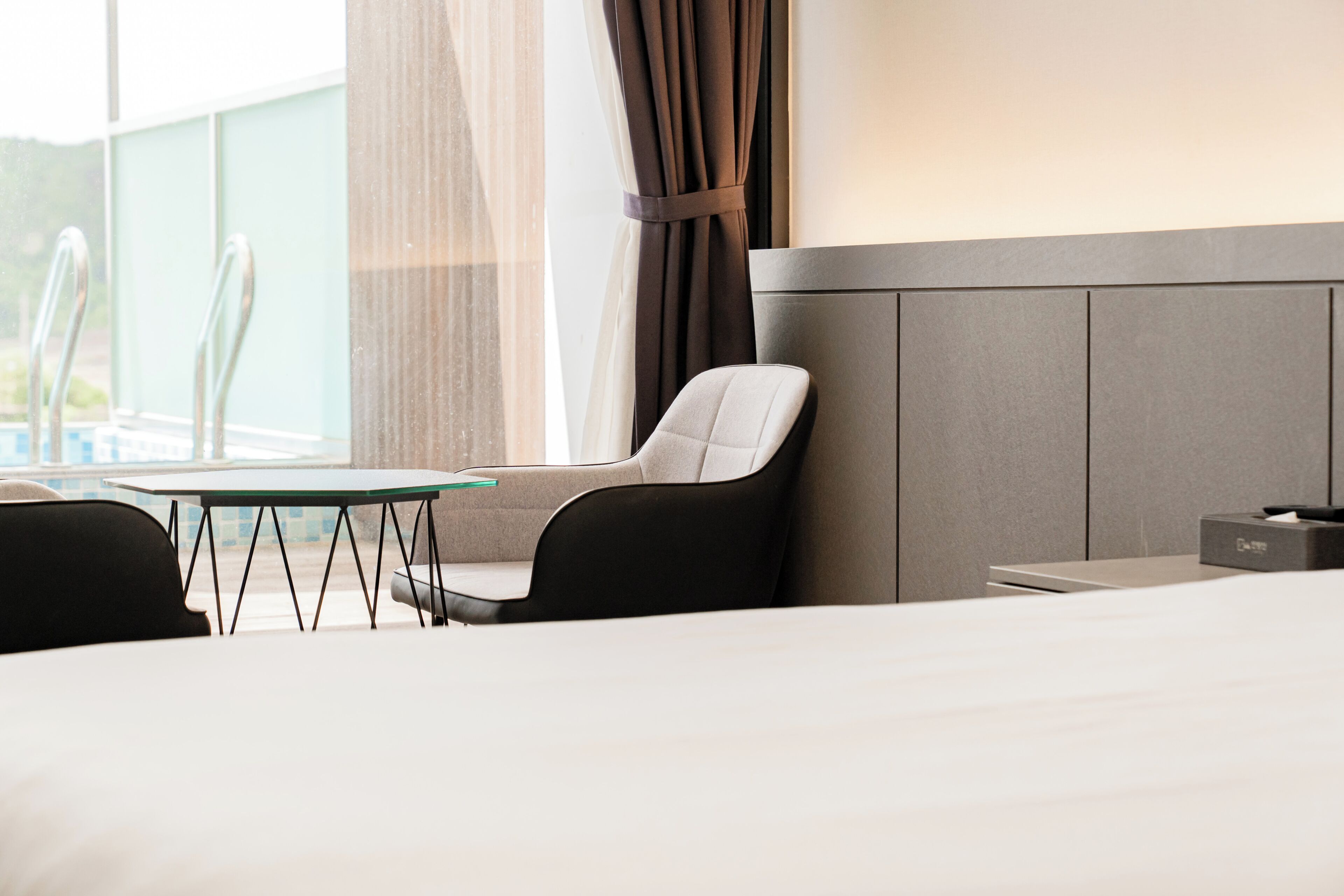 A hotel room with a bed, a table, two chairs, a window with curtains, and a nightstand with a lamp.