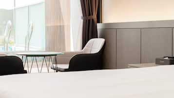 A hotel room with a bed, a table, two chairs, a window with curtains, and a nightstand with a lamp.