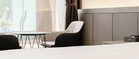 A hotel room with a bed, a table, two chairs, a window with curtains, and a nightstand with a lamp.