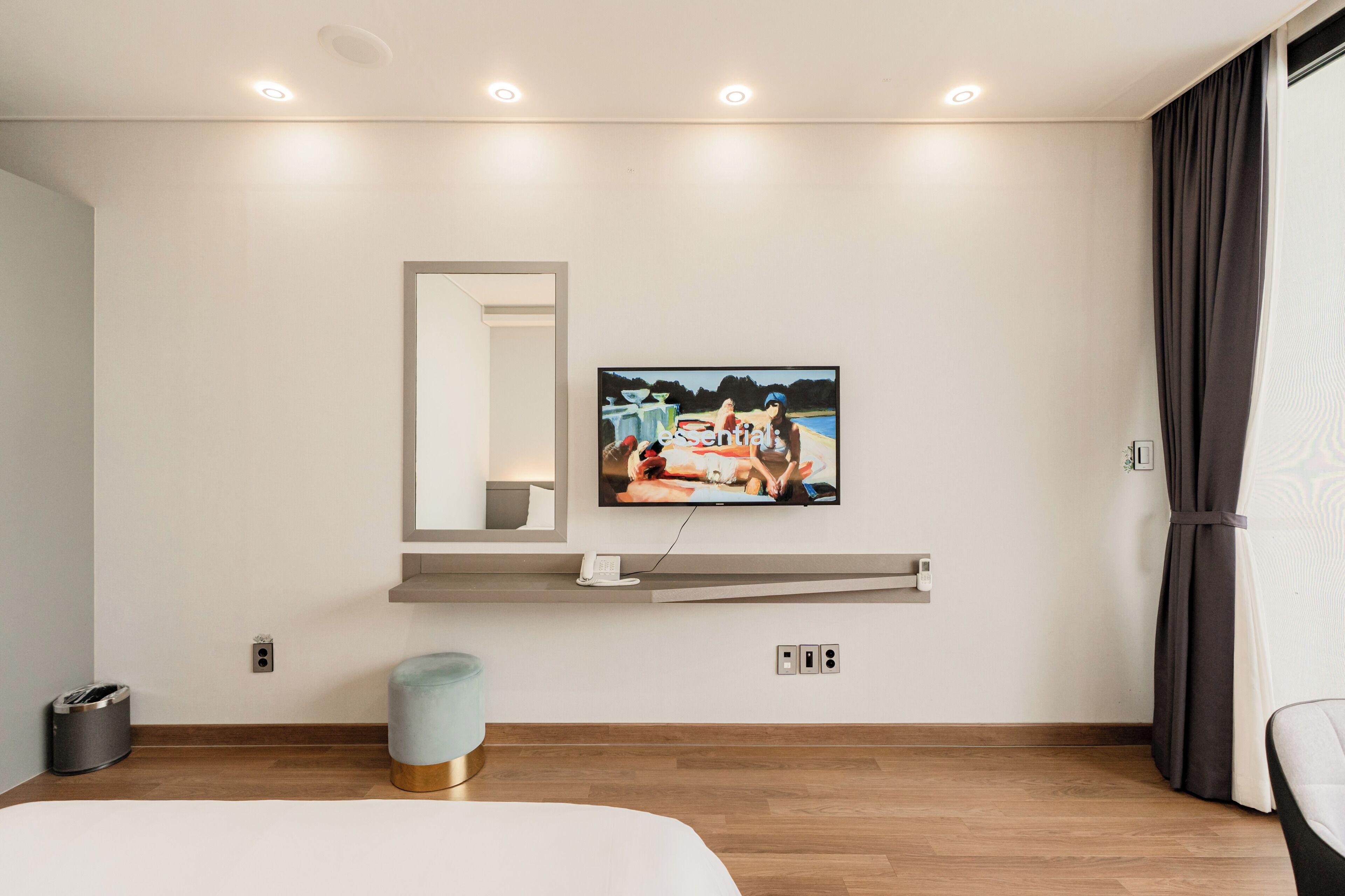 Una habitación de hotel moderna con una televisi ón montada, una mesita de noche, un espejo y suelo de madera.