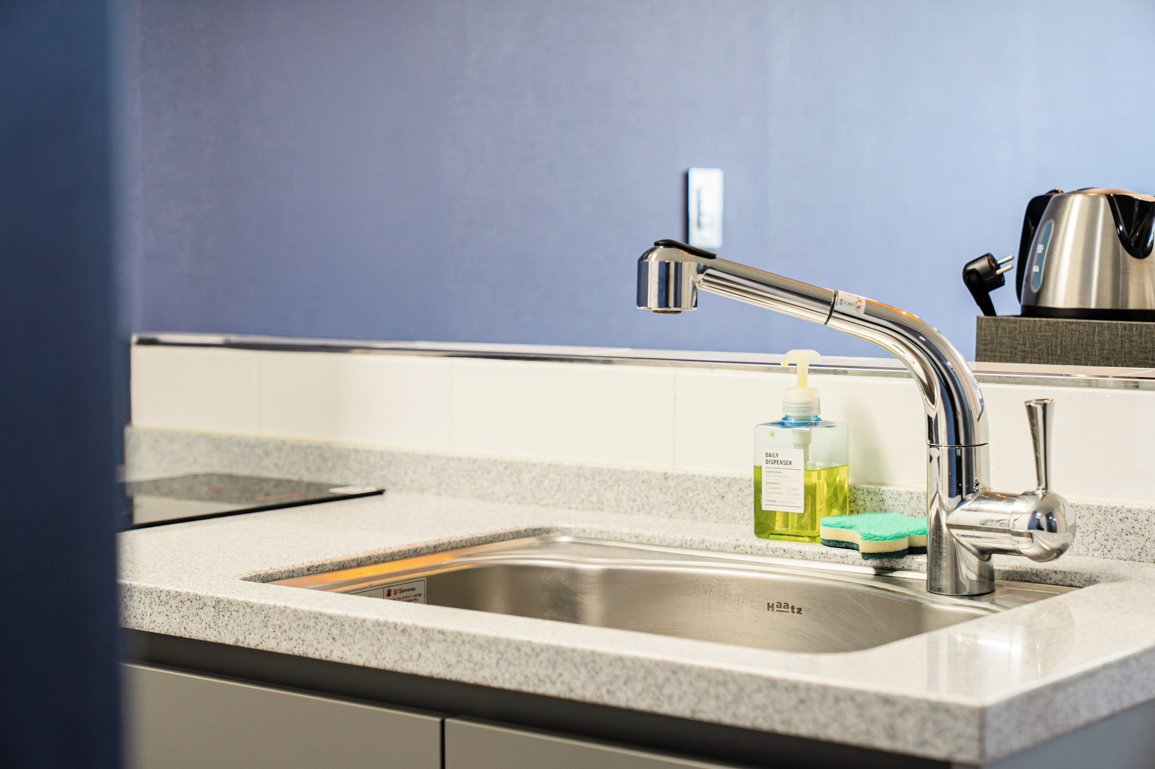 A kitchen sink with a modern faucet, a soap dispenser, and a kettle on the countertop.