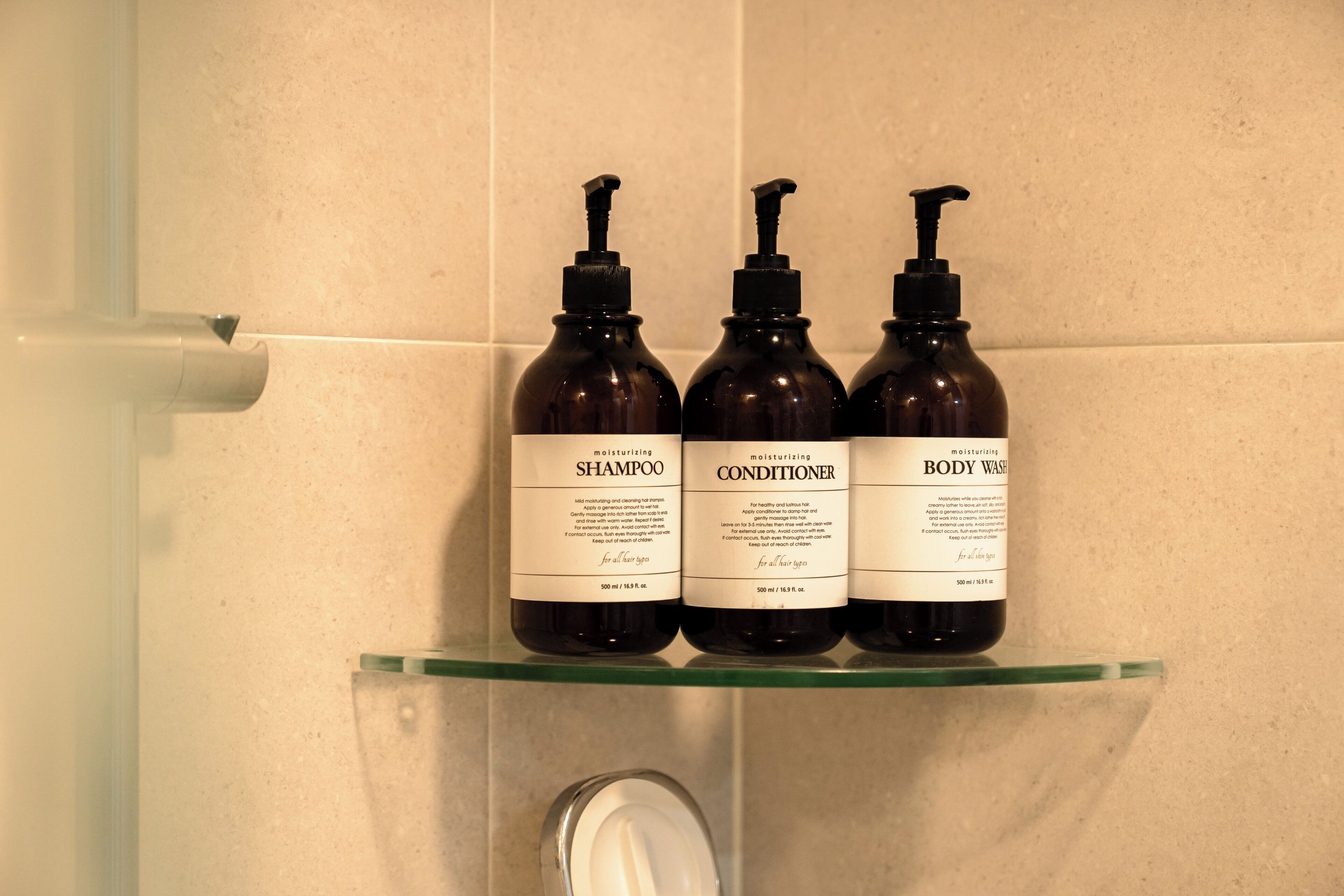 Três frascos de produtos para cabelo numa prateleira de vidro em uma casa de banho.