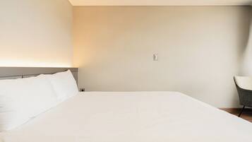 Habitación de hotel minimalista con una cama grande, una silla y una lámpara de pared.