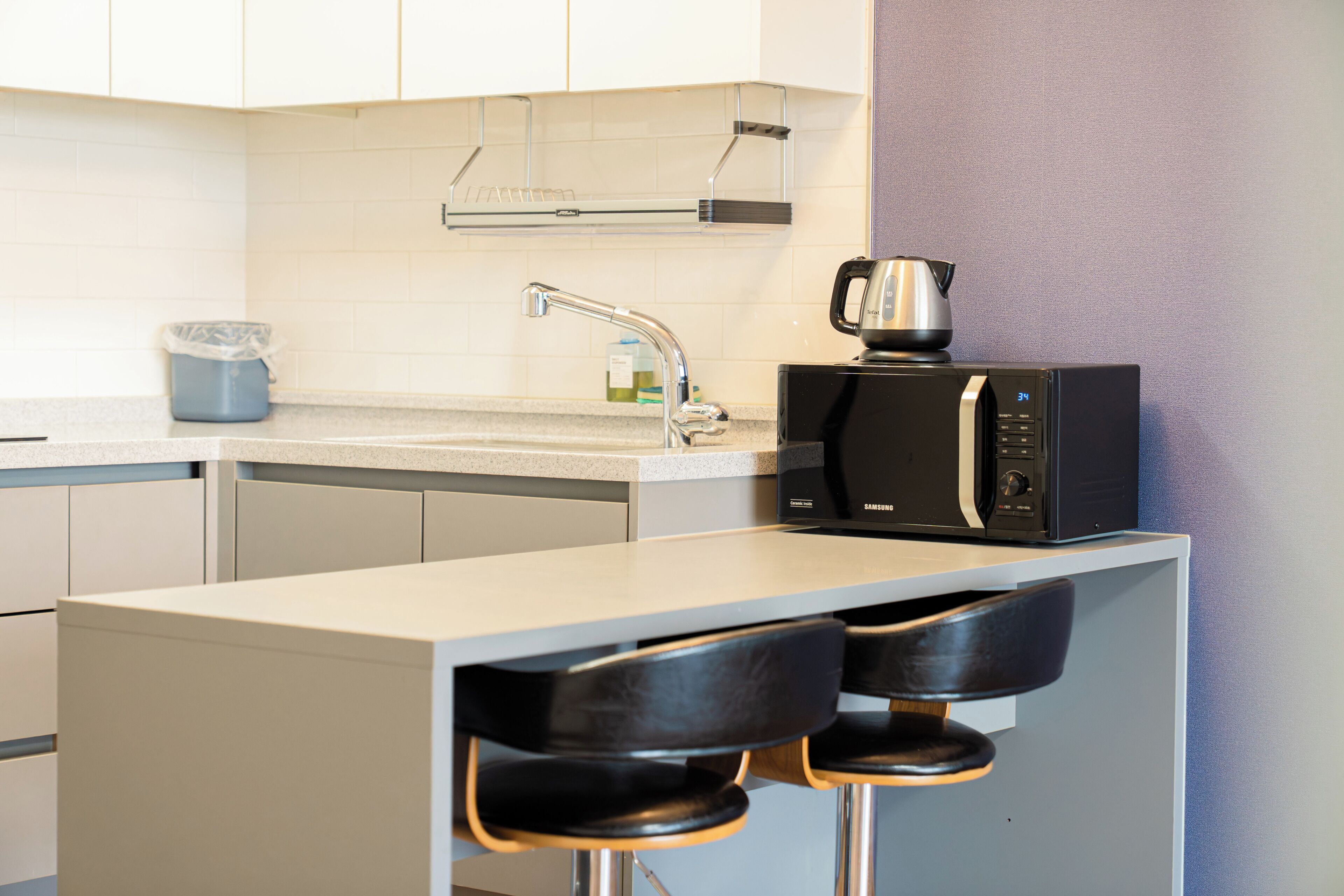 Een moderne keuken met een magnetron, waterkoker en barstoelen.