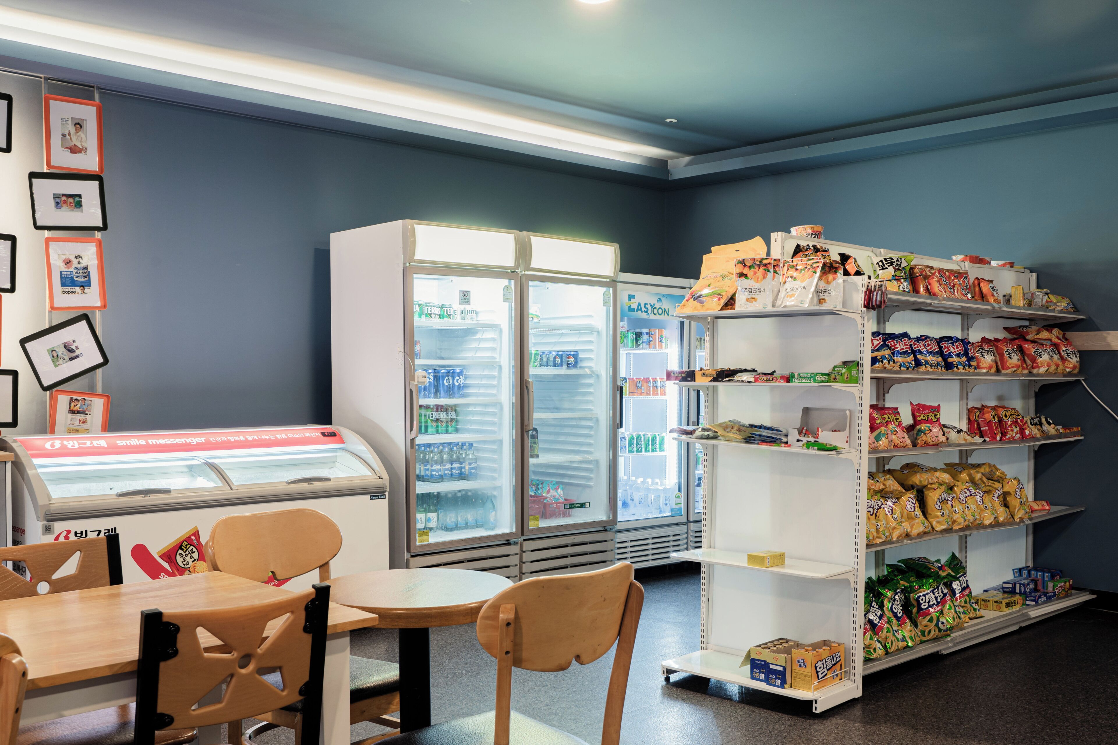 Zona de bar con aperitivos y asientos, un refrigerador lleno de bebidas y estantes con bocadillos envasados.