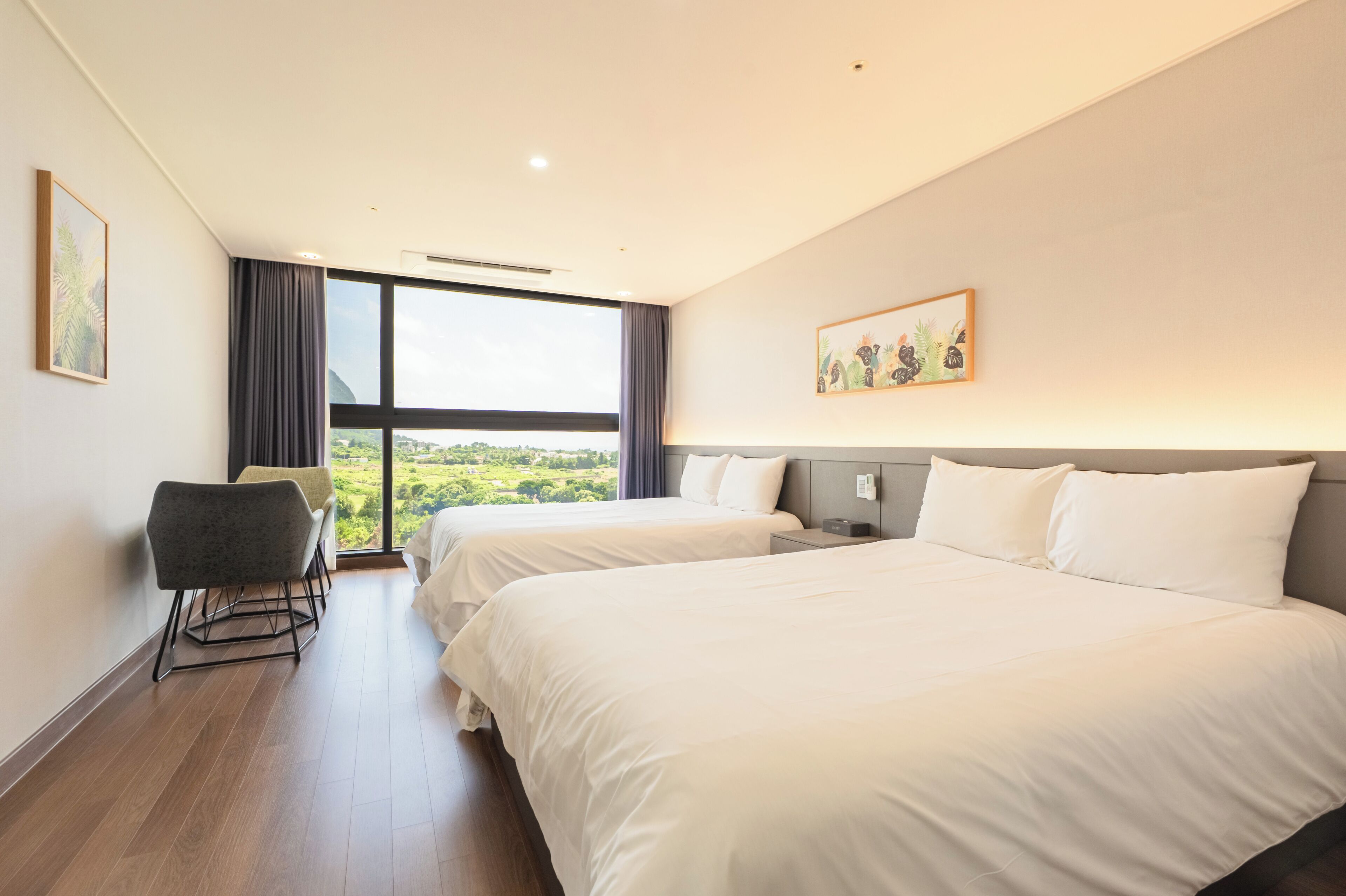 Habitación de hotel con dos camas, un escritorio, una silla y un ventanal con vistas al campo.