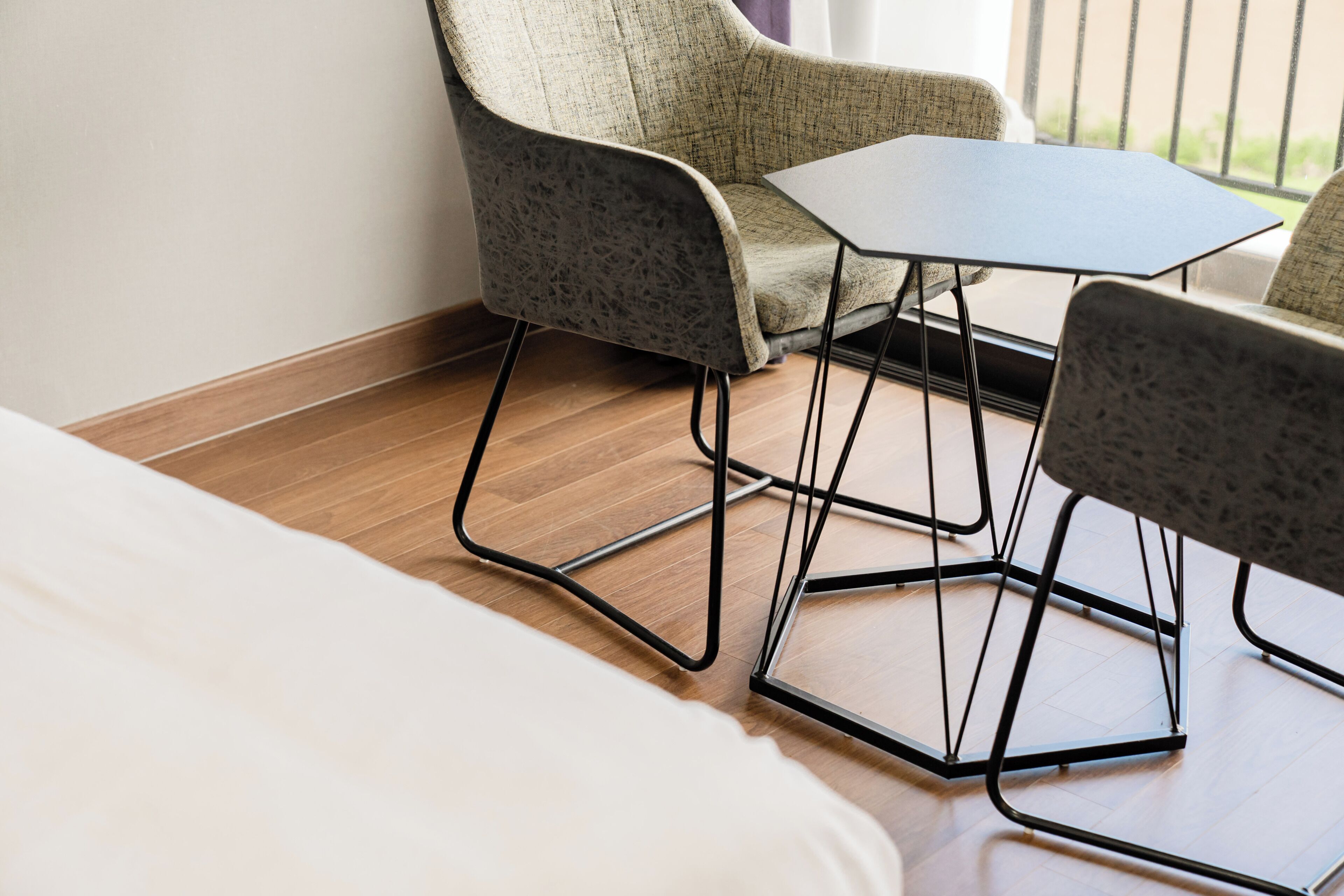 A hotel room with a bed, two chairs, a small table, and a view of the outdoors.