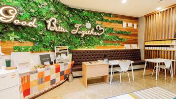 Un área de recepción con una pared verde, un letrero que dice 'Good Better Together', un mostrador de recepción, un espacio de espera con un sofá marrón y una mesita de centro.