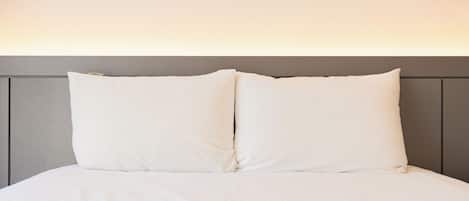 Un lit avec une tête de lit grise et du linge de lit blanc.