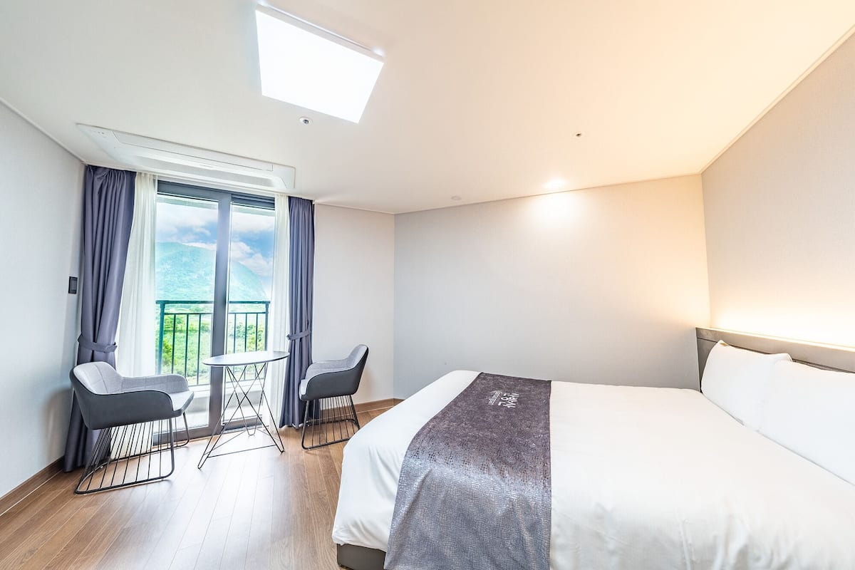 Une chambre d’hôtel comprenant un lit, une petite table, deux chaises, un balcon avec des rideaux et une vue sur l’extérieur.