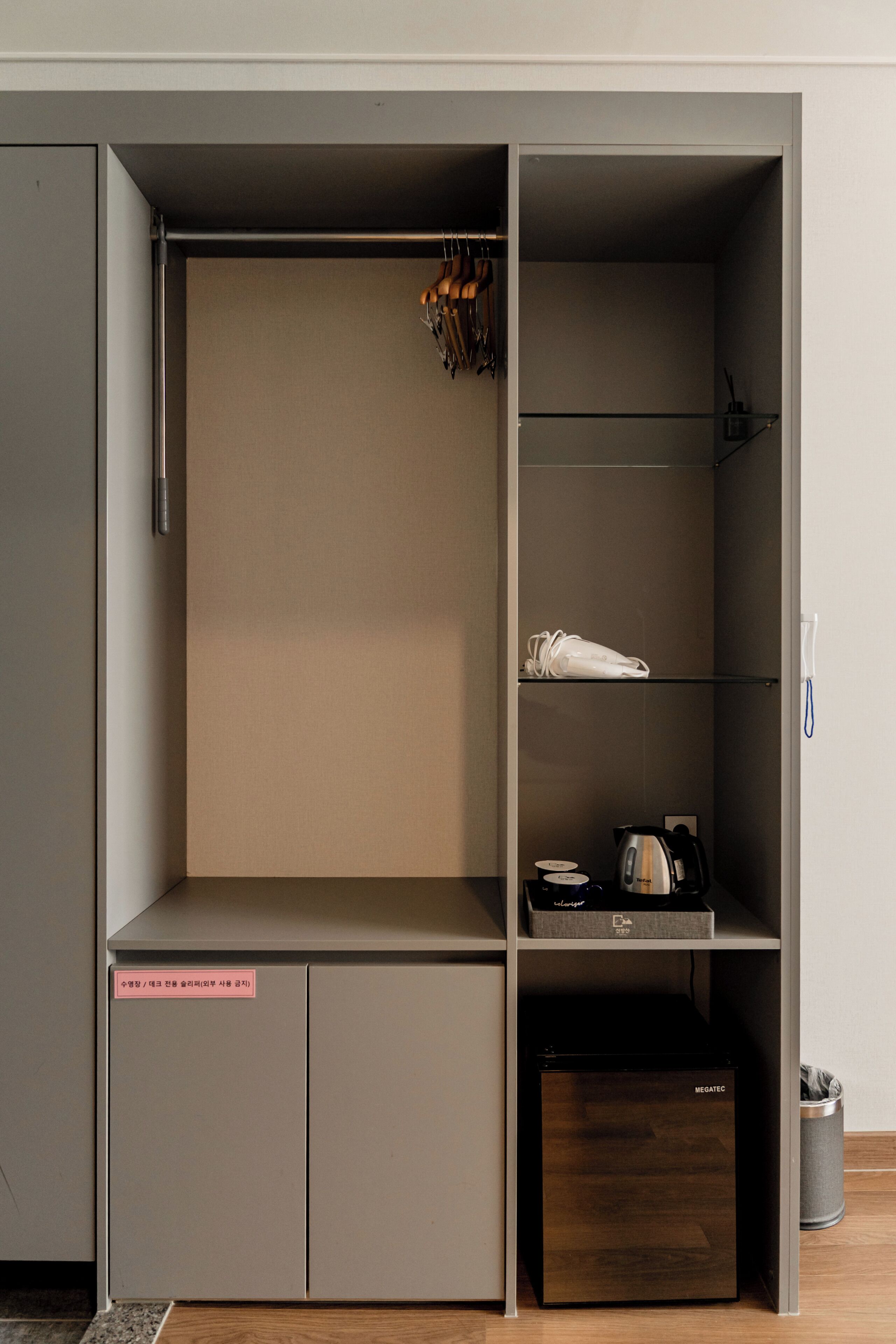 A wardrobe with a mirror, a hanging rack, and a shelf with a kettle and cups.