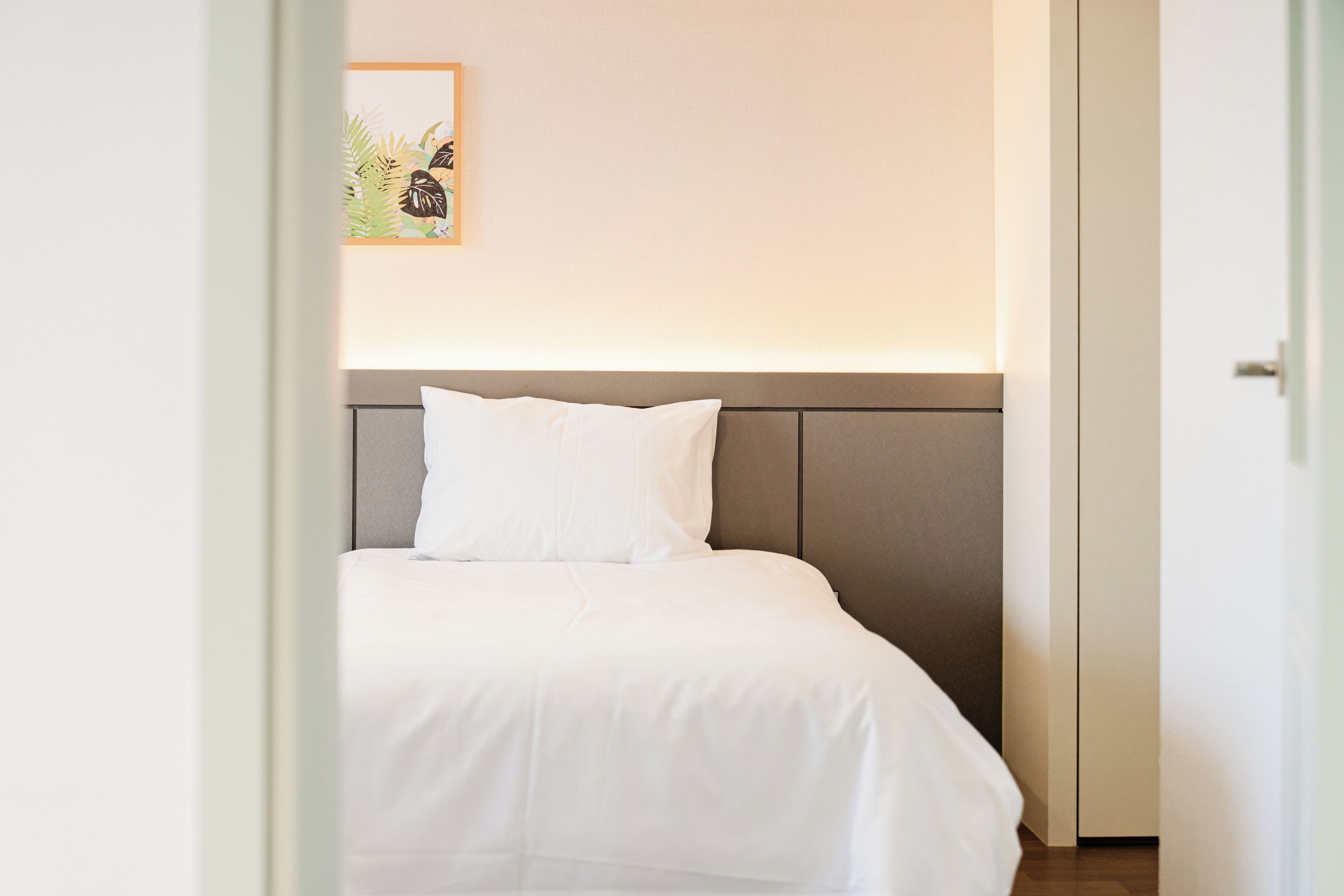 A neatly made bed with a headboard, a framed picture on the wall, and a partially open door.