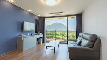 A modern living room with a sofa, a coffee table, a TV mounted on the wall, and a balcony with a mountain view.