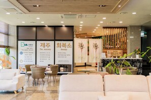 A reception area with a reception desk, seating area with chairs, and informational posters. - Sanbangsan Hotel (Seogwipo)