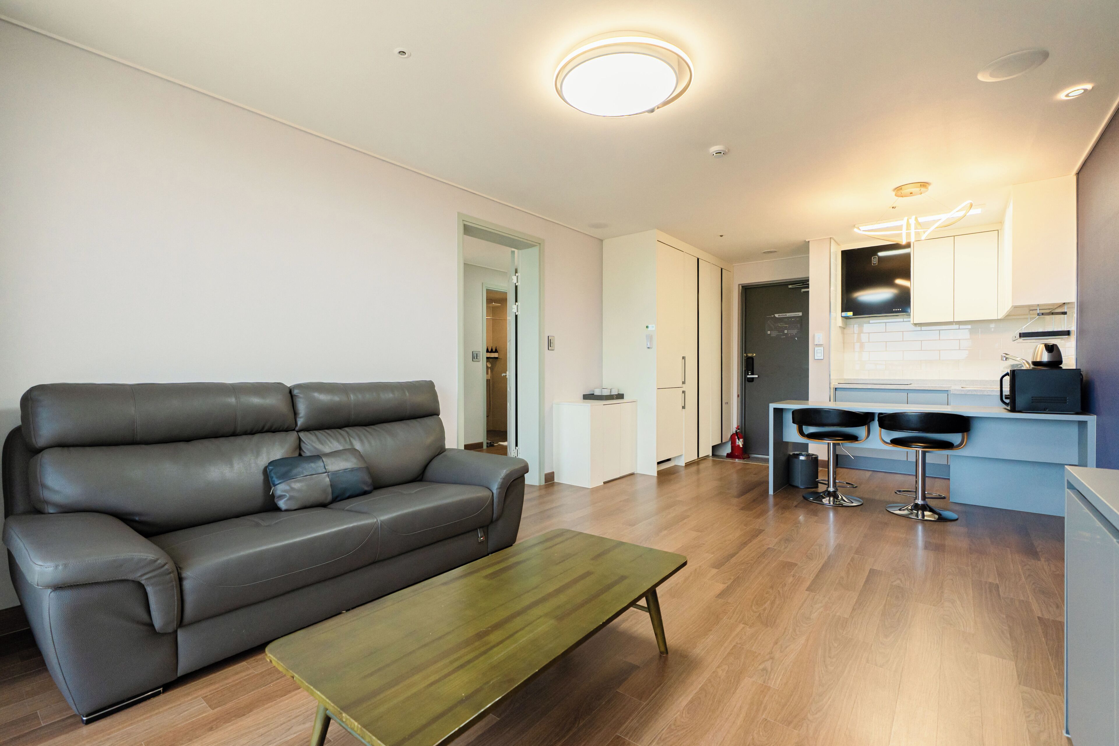 A modern living room with a leather sofa, a wooden coffee table, and a kitchen area with a bar stool.