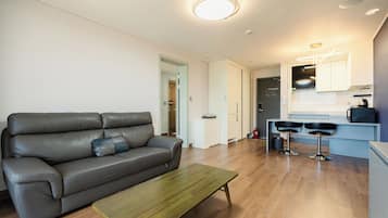 Una sala de estar moderna con un sofá de cuero, una mesa de centro de madera y una zona de cocina con un taburete de bar.