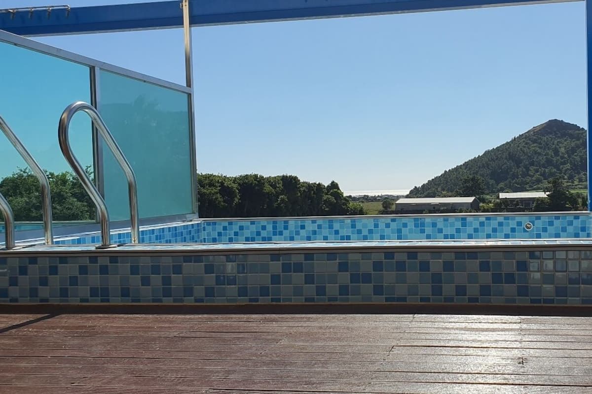 Une piscine aux carreaux de mosaïque bleus, une terrasse en bois et une vue sur une montagne.