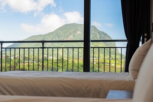 Una cama con vista a una montaña, a través de la barandilla del balcón.