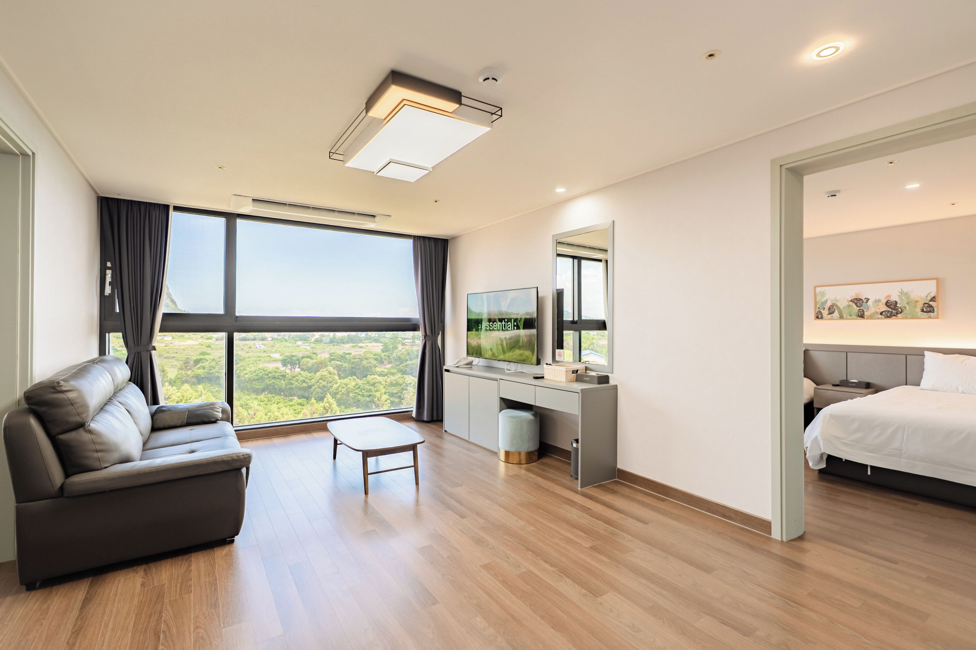 Een moderne hotelkamer met een bank, een bureau met een flatscreen televisie, een bed en een groot raam met uitzicht op het landschap.