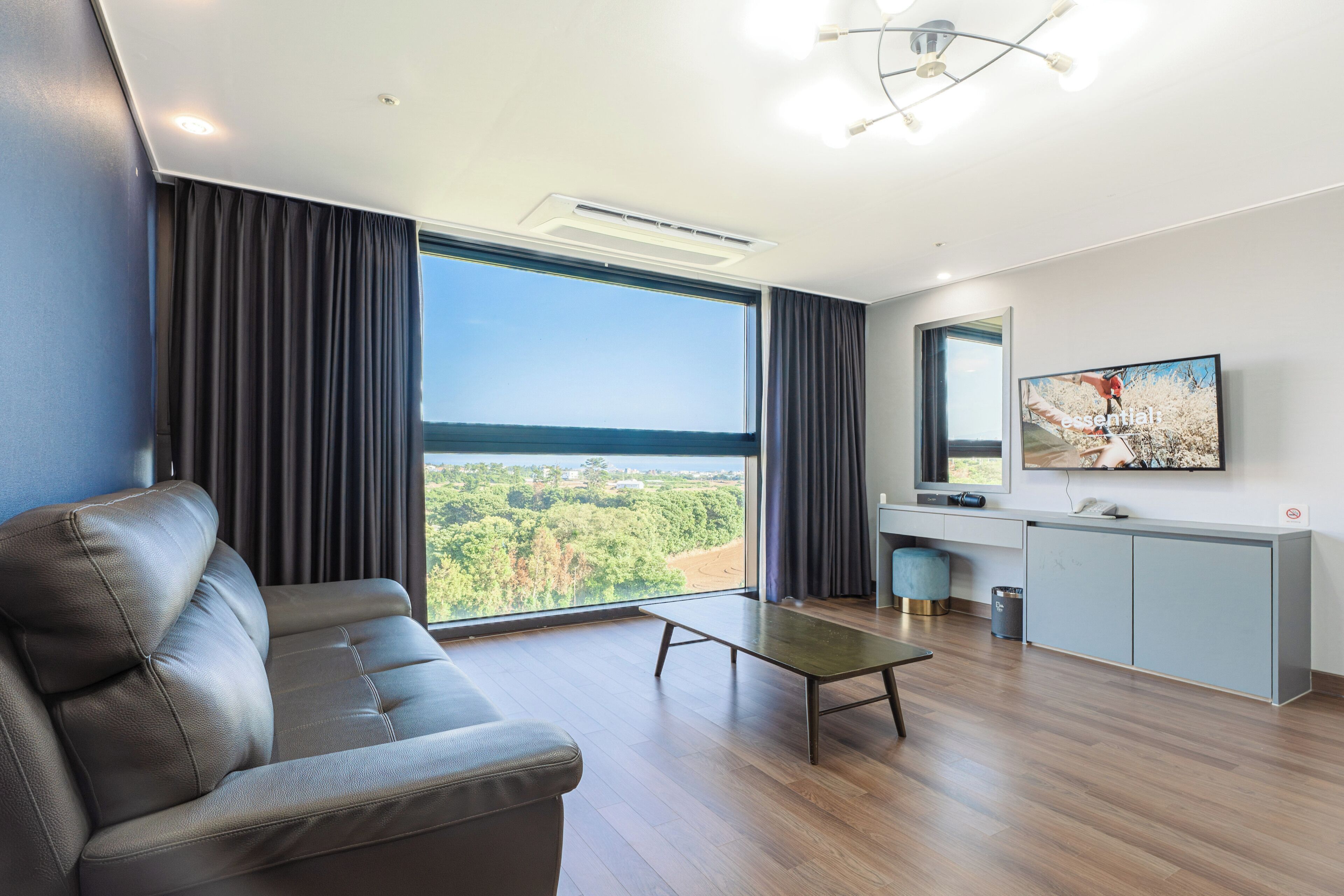 A modern living room with a sofa, a coffee table, a TV, and a view of the outdoors.