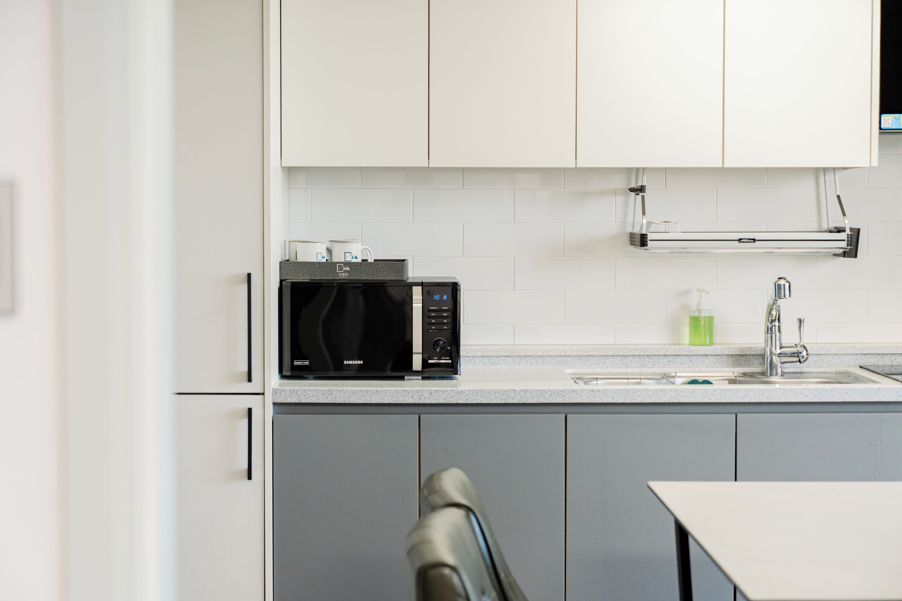 A modern kitchen with white cabinets, a black microwave, and a stainless steel sink.