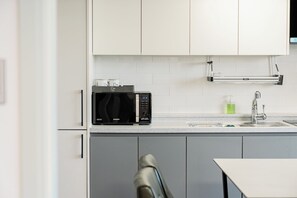 A modern kitchen with white cabinets, a black microwave, and a stainless steel sink. - Sanbangsan Hotel (Seogwipo)